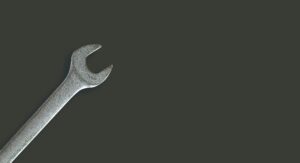 A silver open-end wrench positioned diagonally from the bottom left corner against a plain dark gray background, symbolizing the essential tools for digital marketing, with ample empty space on the right.