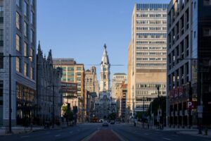 A wide street in a city lined with tall buildings, leading to a historic structure with a clock tower and statue on top, under a clear blue sky—an inspiring setting for any digital marketing or social media management campaign.