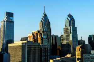 Philadelphia skyline with modern skyscrapers and older buildings under a clear blue sky in daylight. The sun casts shadows on angular glass towers, reflecting the city’s dynamic energy—perfect for a digital marketing or social media management campaign.