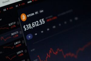 A computer screen displays a cryptocurrency trading platform with the Bitcoin value at $38,612.55. Red line graphs indicate price drops, and other cryptocurrencies with negative percentages are listed on the left, all on a sleek web site design.