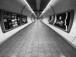 A black and white photo of an empty, tiled underground tunnel with curved walls lined with posters advertising music albums—an inspiring scene for web site design or digital marketing by a creative marketing agency. The tunnel evokes depth and symmetry.