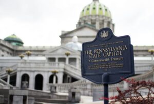 A historical marker in front of the Pennsylvania State Capitol in Harrisburg displays information about the building, with the capitol’s green dome visible in the background—an inspiring sight for any marketing agency or web site design team seeking creative vision.
