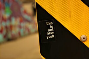 A close-up of a black and yellow street sign with a sticker that reads, this is not new york, in white text. The blurred background reveals colorful graffiti—perfect inspiration for a digital marketing campaign or web site design.