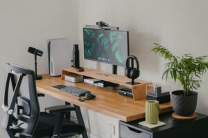 A modern, organized desk setup ideal for social media management, featuring a monitor with a green leafy wallpaper, keyboard, mouse, speakers, water bottle, headphones, potted plant, and stylish accessories on a wooden surface.