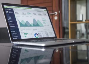 A laptop on a glass table displays a dashboard with graphs, charts, and statistics for website analytics data—essential insights for any digital marketing or social media management team in an office setting.