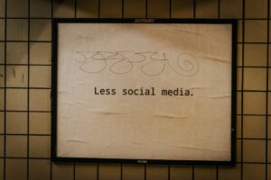 A framed beige sign on a tiled wall reads Less social media., subtly hinting at mindful Social Media Management, with squiggly abstract lines above the text.
