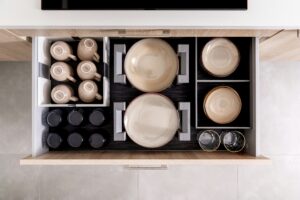 Open kitchen drawer organized with beige cups, plates, and bowls in neat compartments, alongside black tumblers and two smaller glasses—an arrangement as thoughtfully curated as a marketing agency approaches web site design.