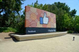 A large outdoor sign featuring a thumbs-up like symbol, patterned background, and text reading facebook and 1 Hacker Way, surrounded by trees and greenery—an iconic spot often visited by marketing agency teams and digital marketing experts.