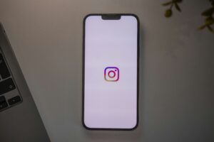 A smartphone displaying the Instagram logo on its screen rests on a light-colored surface next to part of a laptop keyboard—an ideal setup for social media management and digital marketing tasks.
