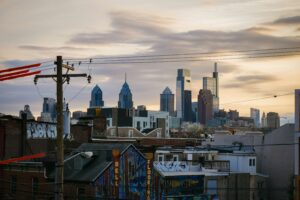 Philadelphia skyline at sunset with tall modern buildings in the background, residential rooftops and colorful graffiti in the foreground, power lines crossing the scene—an inspiring view for any marketing agency or web site design project.